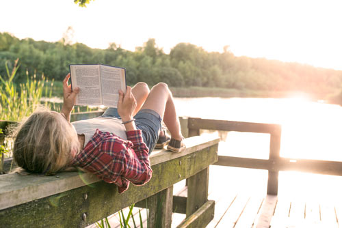 En person ligger på en brygga och läser en bok i kvällssolen