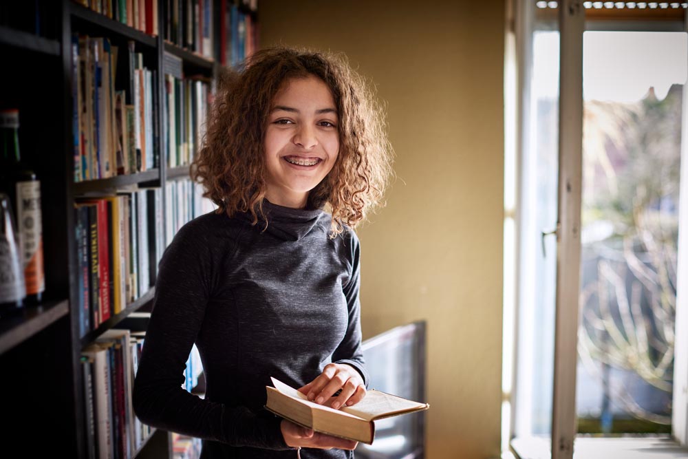En glad tjej med tandställning håller i en uppslagen bok